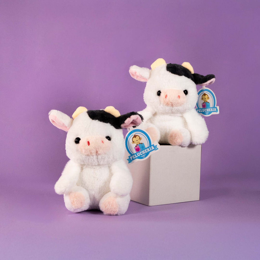 Dos pequeñas vacas de peluche blancas sentadas sobre fondo morado
