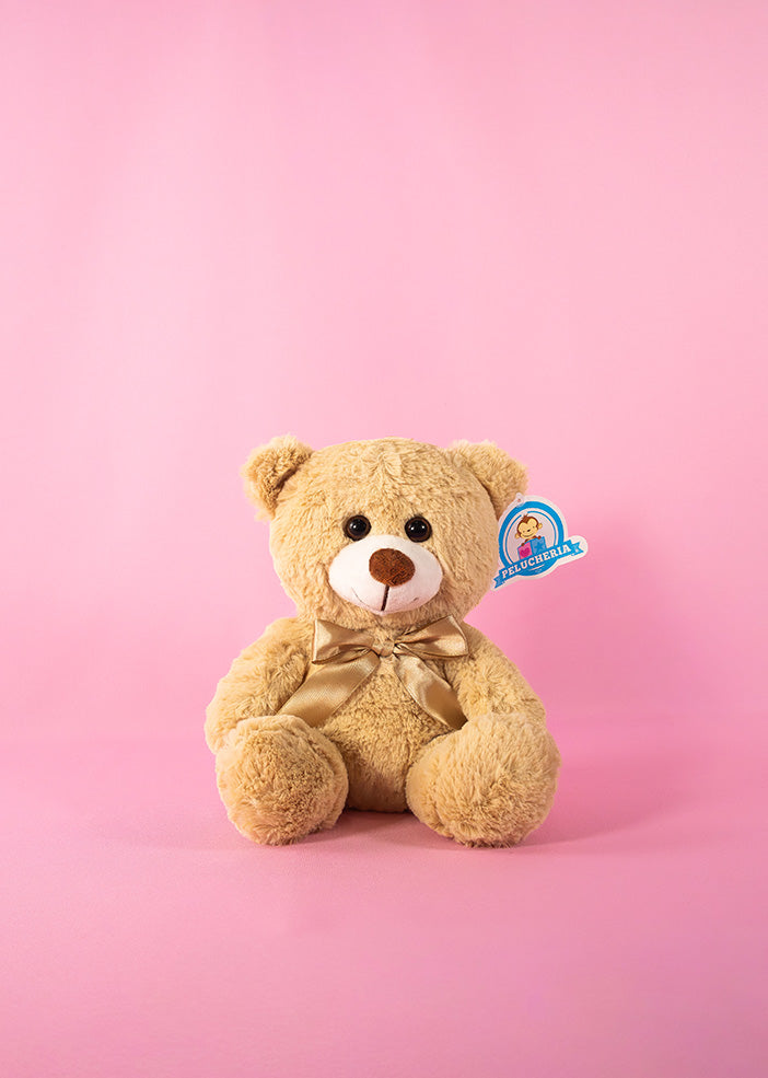 Oso de peluche beige con nariz roja y corazones en las patas sobre un fondo rosa