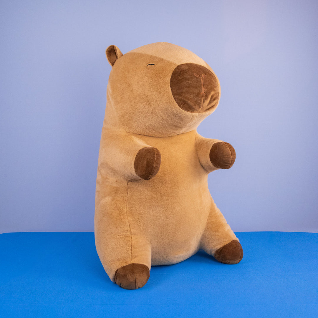 Capibara de peluche grande color café claro de pie sobre fondo azul