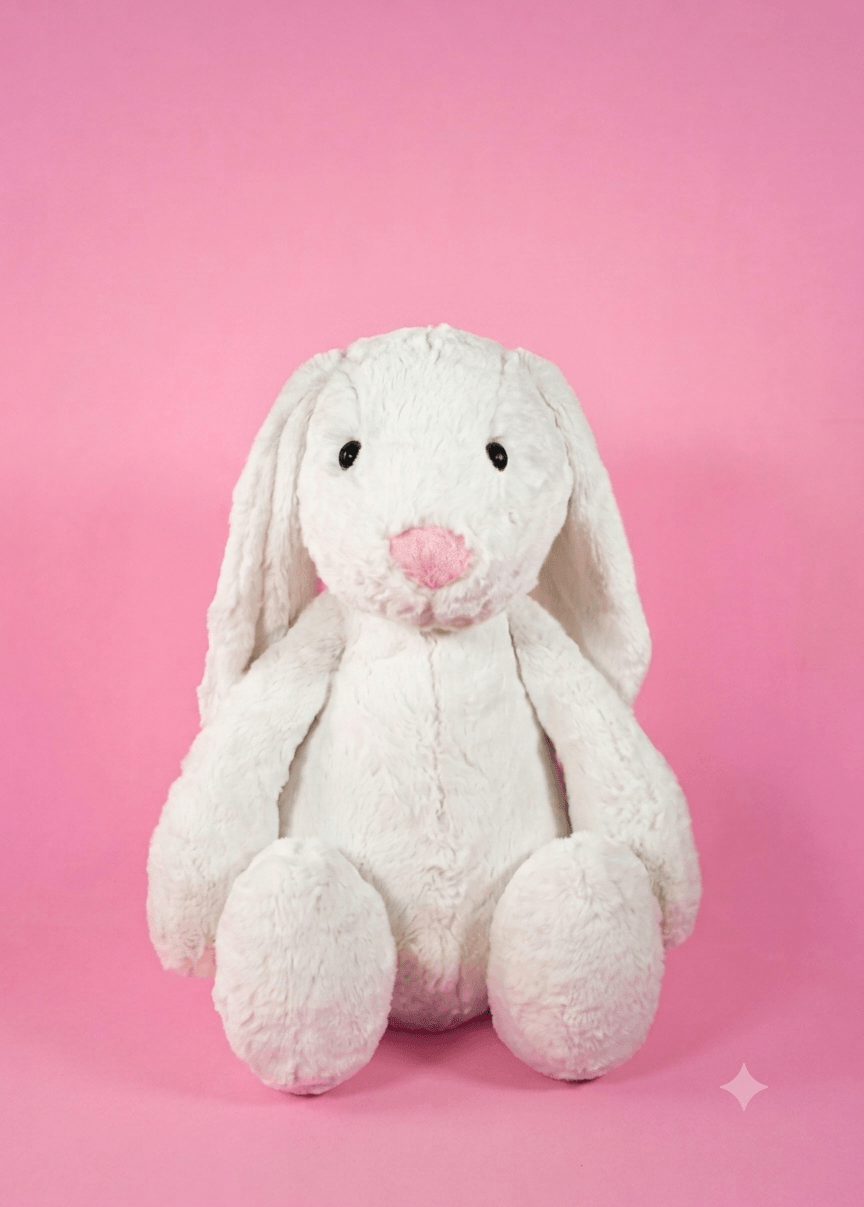 Peluche de conejo blanco sentado con orejas caídas sobre fondo rosa