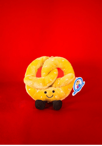 Peluche en forma de pretzel sonriente color amarillo sobre fondo rojo