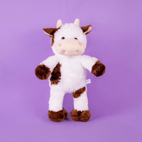 Vaca de peluche color crema de pie sobre fondo morado