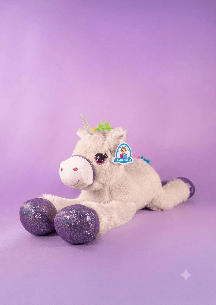 Peluche de unicornio blanco recostado con patas brillantes sobre fondo morado