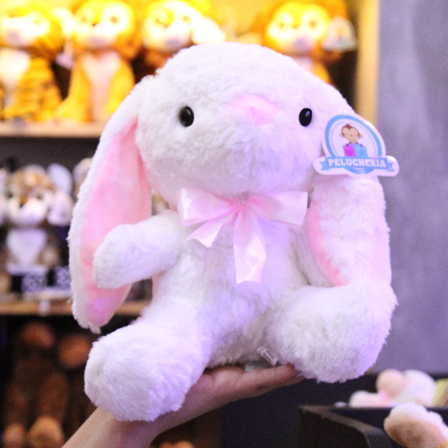 Conejo de peluche blanco con orejas largas, felpa suave y moño decorativo.