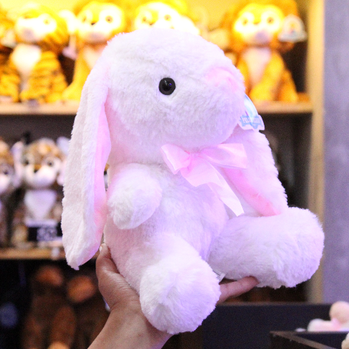 Conejo de peluche blanco con orejas largas, felpa suave y moño decorativo.