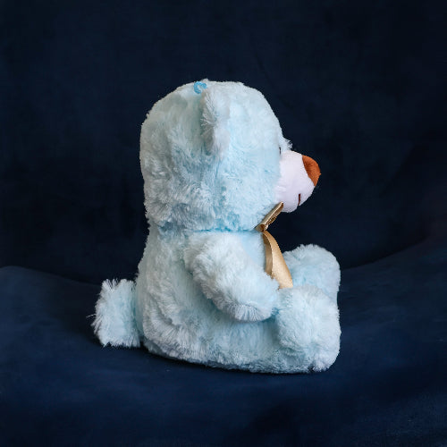 Oso de peluche color azul claro, de felpa suave, sentado y con moño decorativo.