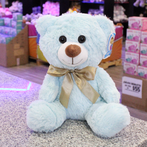 Oso de peluche color azul claro, de felpa suave, sentado y con moño decorativo.