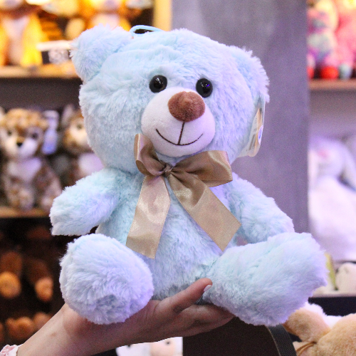 Oso de peluche color azul claro, de felpa suave, sentado y con moño decorativo.