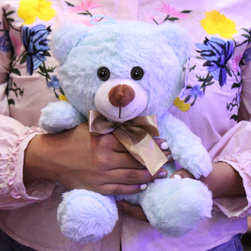 Oso de peluche color azul claro, de felpa suave, sentado y con moño decorativo.