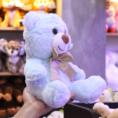 Oso de peluche color azul claro, de felpa suave, sentado y con moño decorativo.