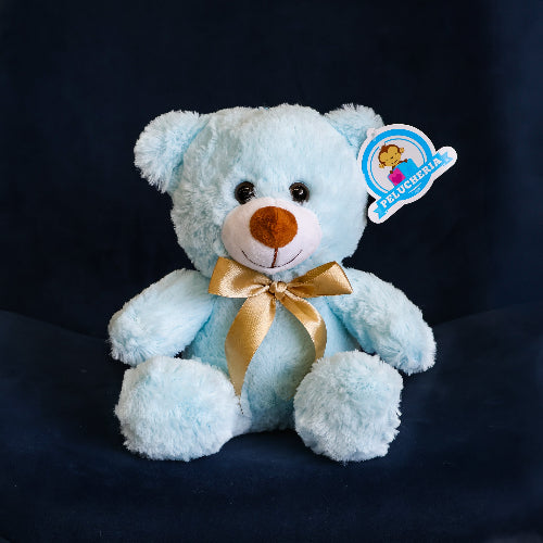 Oso de peluche color azul claro, de felpa suave, sentado y con moño decorativo.