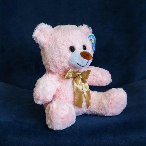 Oso de peluche color rosa con moño decorativo, ideal para regalo romántico o infantil.