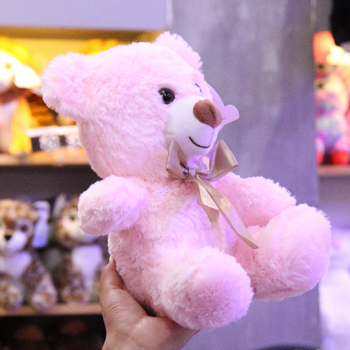 Oso de peluche color rosa con moño decorativo, ideal para regalo romántico o infantil.